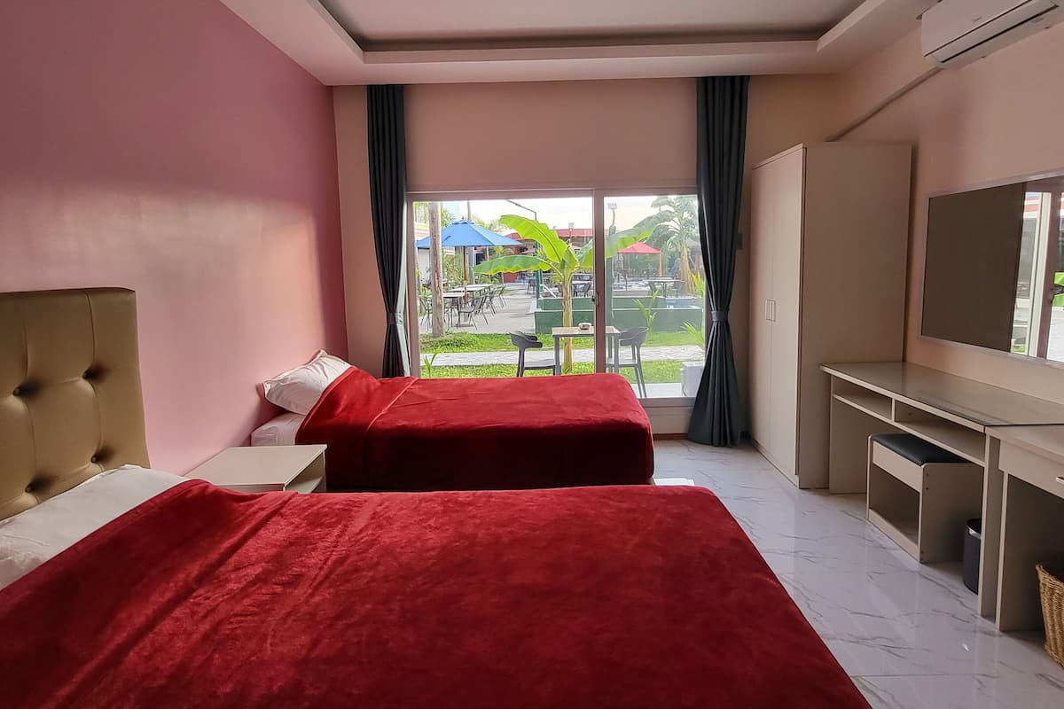 Quarto de hotel com duas camas, televisão, escrivaninha e uma janela grande com vista para a área externa.