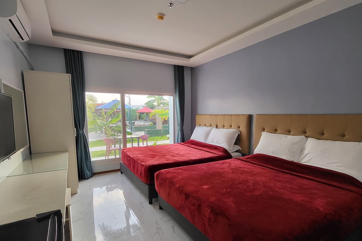 Quarto de hotel com duas camas, televisão, escrivaninha e porta de vidro deslizante para área externa.