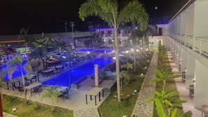 An outdoor pool area with seating and tables, surrounded by palm trees and a building with a modern design. - Blue Hotel & Resort (Porac)