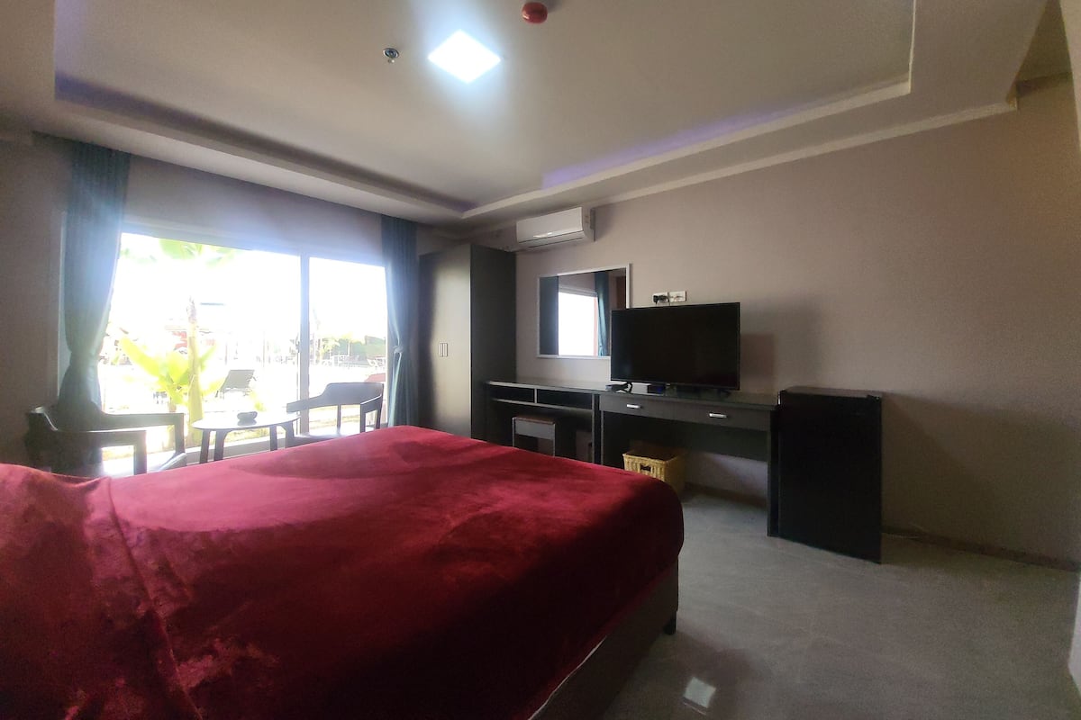 Quarto de hotel com cama, escrivaninha, televisão e janela com vista para o exterior.