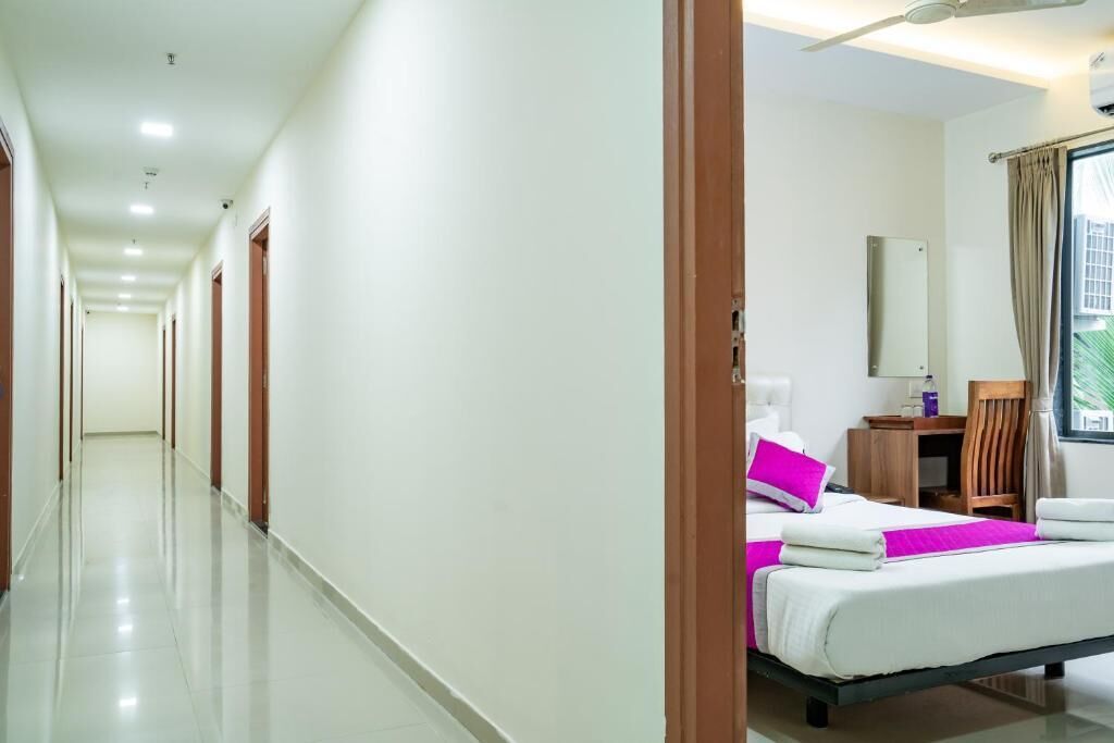 A hotel corridor with a bed, bedside table, and a window with curtains.