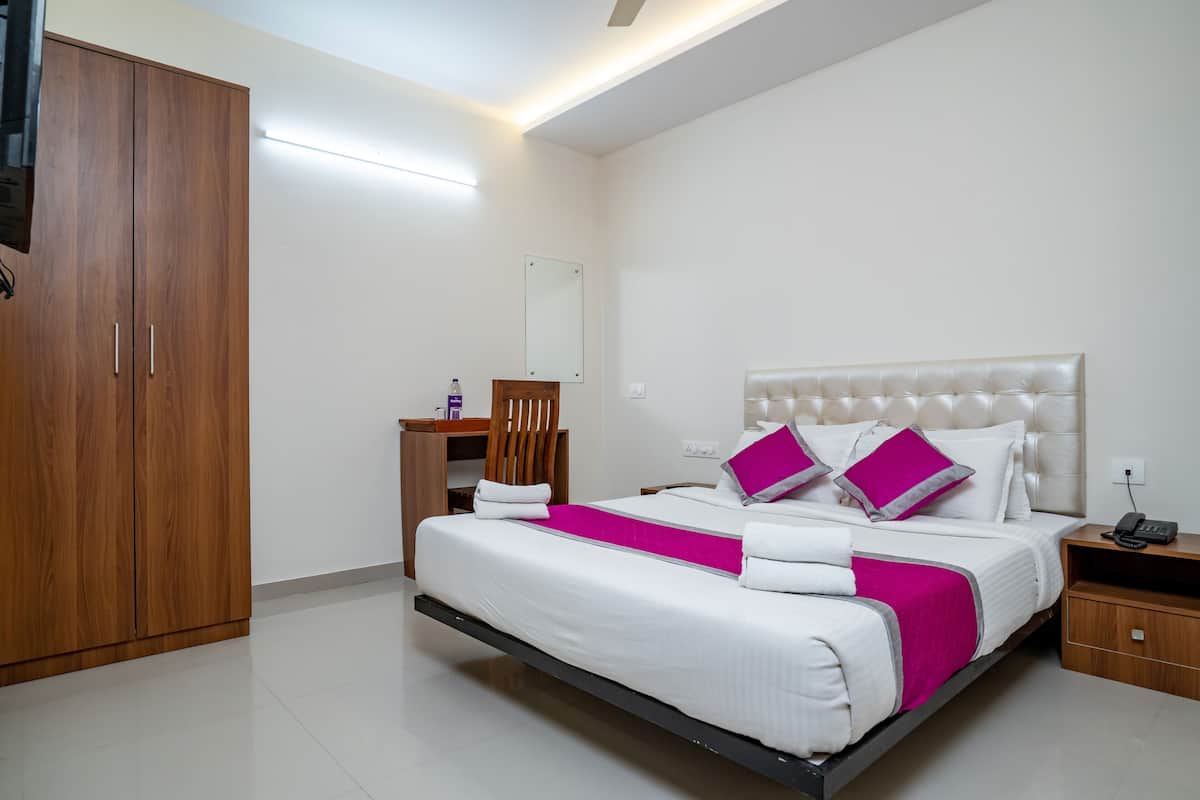 A modern hotel room with a large bed, a wardrobe, a desk, and a mirror.