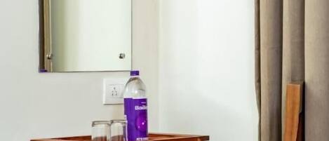 Un pequeño escritorio de madera con un espejo encima, una botella de jabón para manos y un par de gafas.
