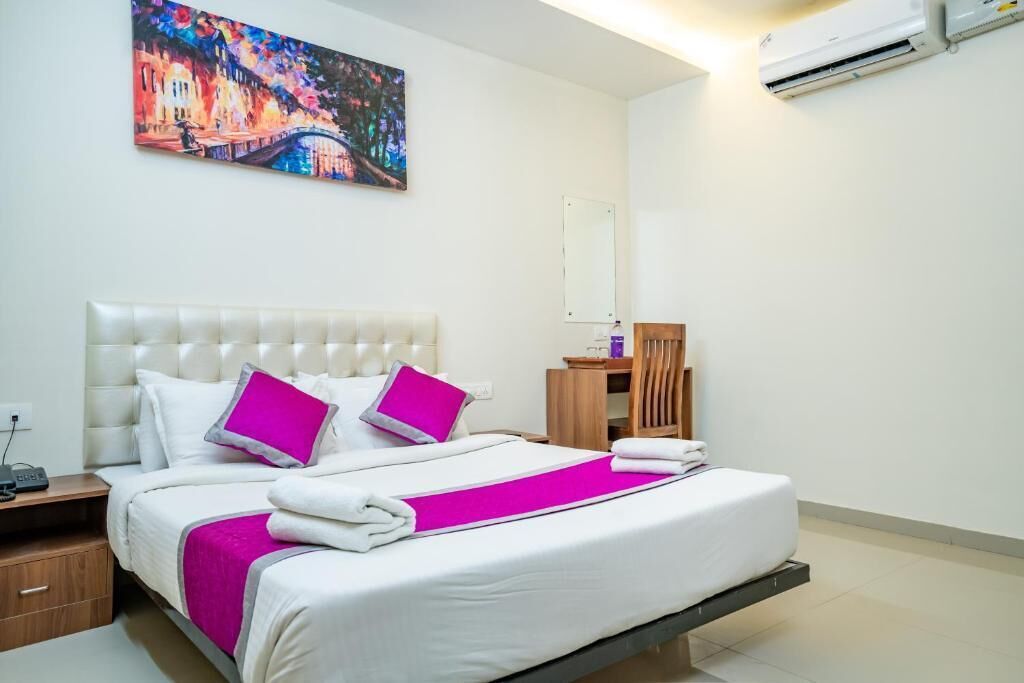 Una habitación de hotel con una cama grande, una mesita de noche, una silla de madera, un espejo y un equipo de aire acondicionado.