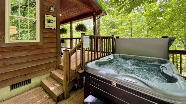 En stuga av trä med ett bubbelbad på terrassen, en skylt som visar vägen till en utsiktsplats i Appalacherna och en utsikt över frodig grönska.