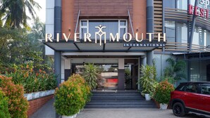 Entrada del hotel RiverMouth International con un coche rojo estacionado afuera, rodeado de plantas en macetas y palmeras.