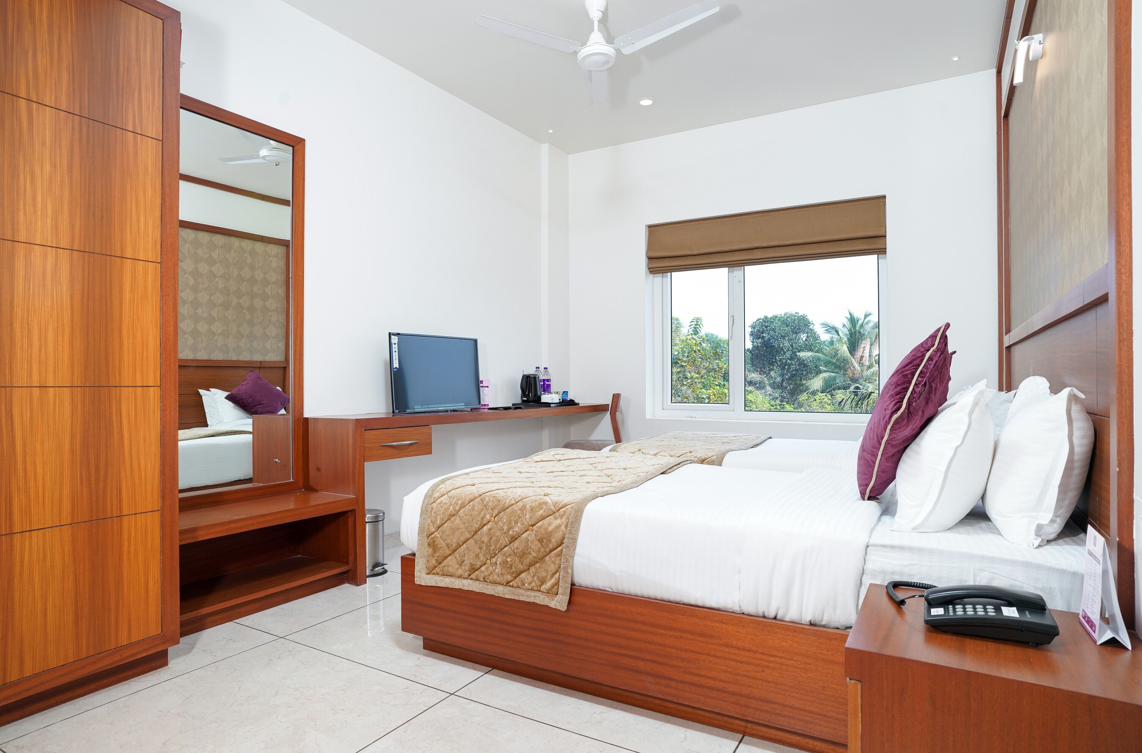 A bedroom with a bed, a desk, a wardrobe, and a window with a view of greenery.