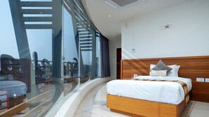 Una habitación de hotel moderna con una cama grande, cabecera de madera y vistas a través de ventanas de gran altura.