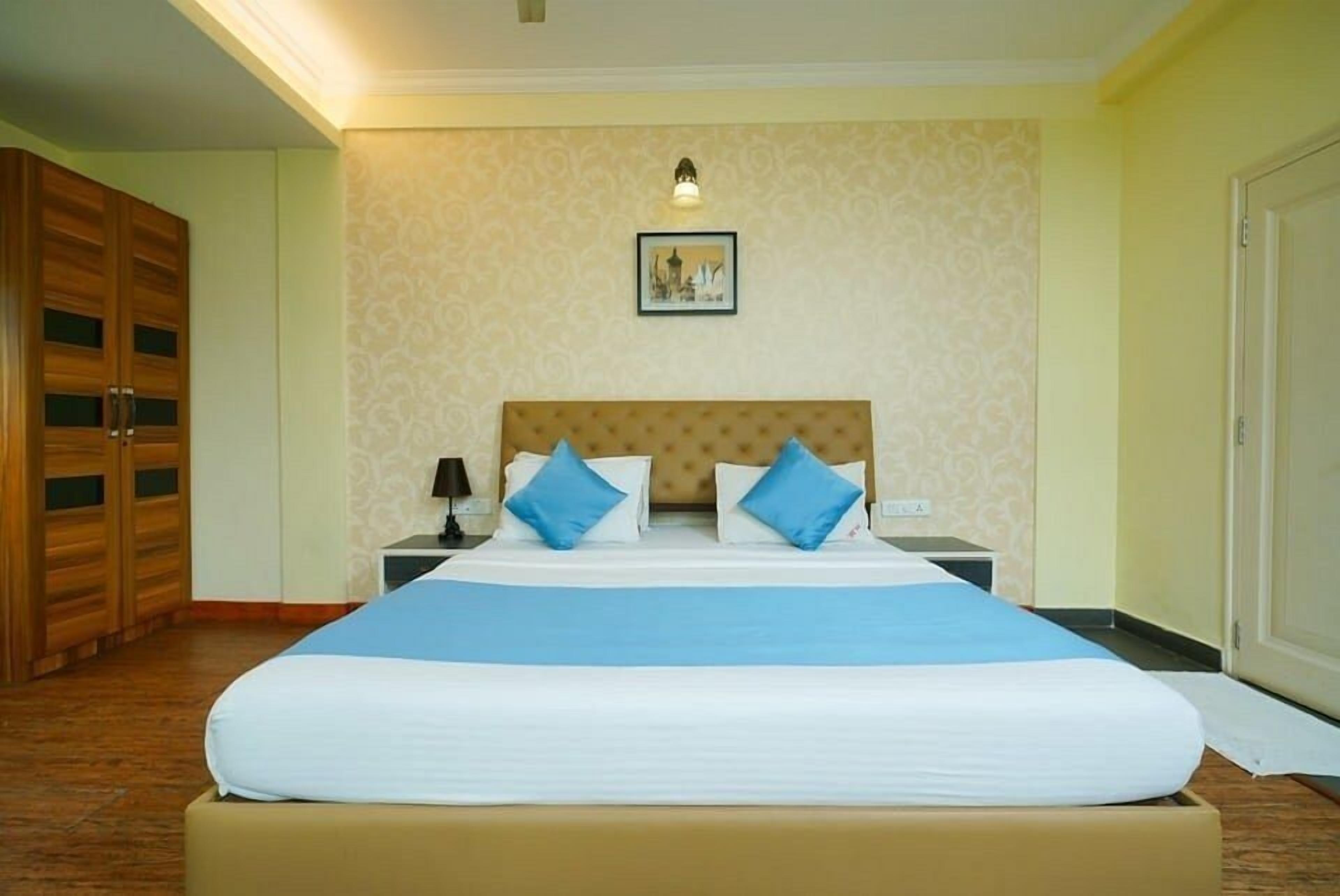 Ein Hotelzimmer mit einem großen Bett, einem Holzschrank, einem Nachttisch mit Lampe und einem gerahmten Bild an der Wand.