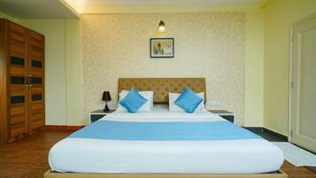 A hotel room with a large bed, a wooden wardrobe, a nightstand with a lamp, and a framed picture on the wall.