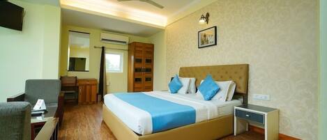 A hotel room with a bed, bedside table, desk, chair, wardrobe, and a ceiling fan.