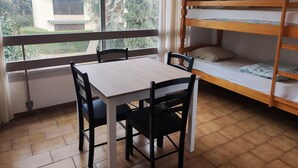 A room with a wooden bunk bed, a table with chairs, and a window with curtains. - Apartment for 5 with Pool, Tennis, Parking - 500m from Beach (Argelès-sur-Mer)