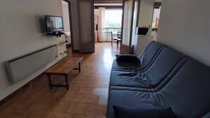 A living room with a sofa, a television, and a small table. There is a door leading to another room. - Apartment for 5 with Pool, Tennis, Parking - 500m from Beach (Argelès-sur-Mer)