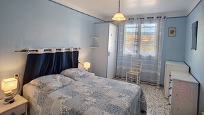 A bedroom with a bed, a chair, a desk, and a window with curtains.