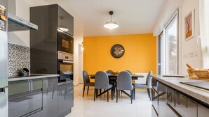 A modern kitchen with grey cabinets, a dining table with chairs, and a yellow accent wall. - Charming House with Garden, Close to Beaches & Guérande, Free WiFi (Assérac)
