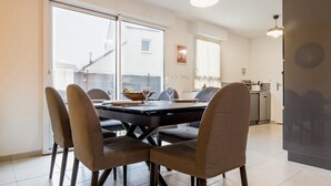 A dining area with a table set for four, surrounded by chairs, in a modern apartment with large windows and a view of the outside. - Charming House with Garden, Close to Beaches & Guérande, Free WiFi (Assérac)