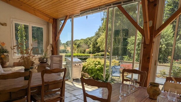 A wooden dining table with chairs, a glass-top table, and a view of a garden through large windows. - Rustic old mill with garden, WIFI and parking, pets allowed (Saint-Mary)
