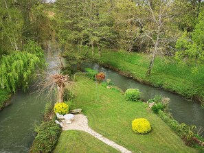 Ein Fluss mit einem Steinweg, einem kleinen Tisch und Stühlen, umgeben von Grünpflanzen und Bäumen.