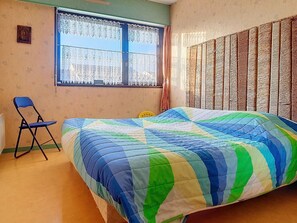 A room with a bed, a chair, a window with lace curtains, and a patterned wall.