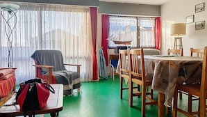 Et værelse med spisebord, stole, sofa, lænestol, lampe og et vindue med gardiner.