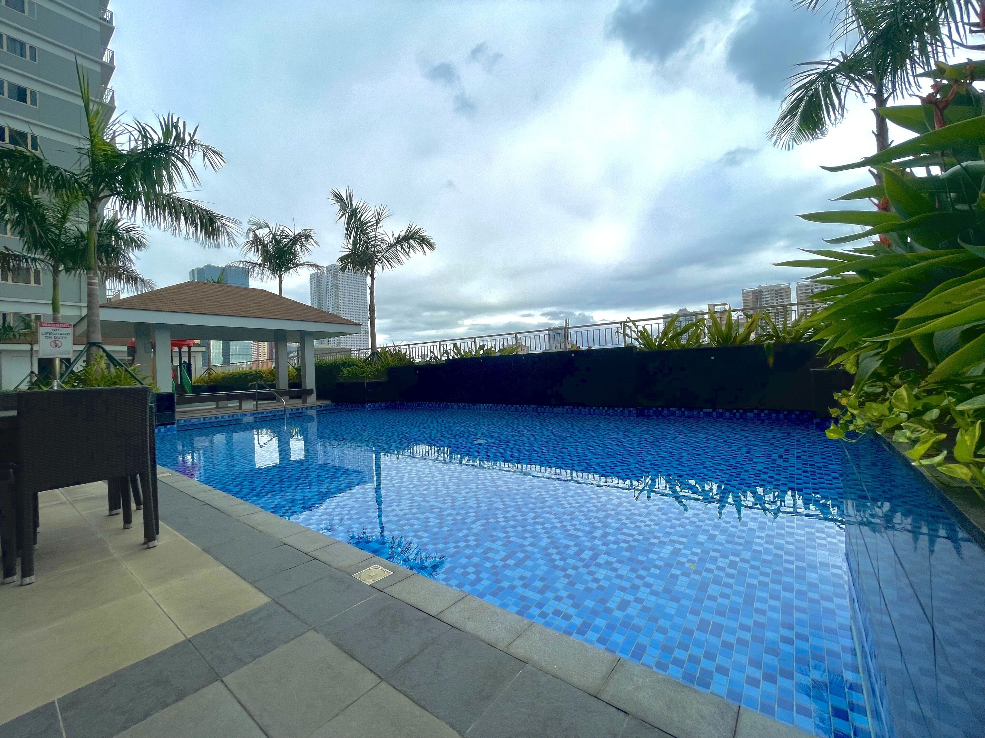 Une piscine dont le fond est recouvert de carrelage, entourée de palmiers et avec un bâtiment visible au loin.