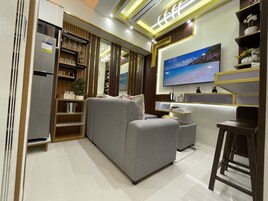 Un salon moderne avec un canapé gris, un téléviseur fixé au mur et une bibliothèque en bois.