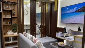 Un salon moderne avec un canapé gris, une table basse et un téléviseur fixé au mur. On y trouve également un meuble en bois avec des étagères et une plante en pot.