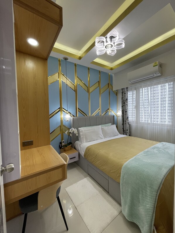 A bedroom with a bed, bedside table, desk, and an air conditioning unit.