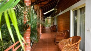 A covered outdoor area with a tiled floor, wicker furniture, and a brick pillar. - Nexstay Coffee Grove Resort (Chikkamagaluru)