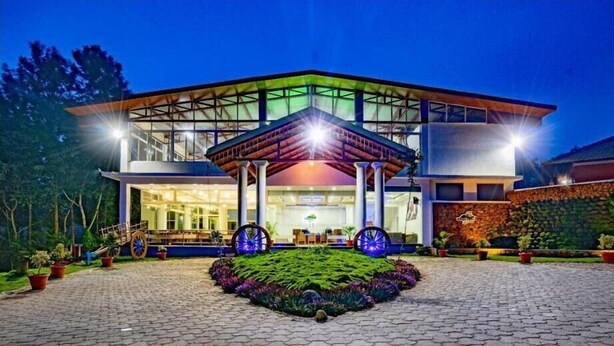 A modern building with a glass facade, a covered entrance, and a landscaped garden with a central circular feature. - Nexstay Coffee Grove Resort (Chikkamagaluru)