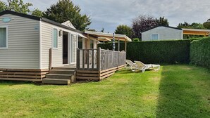 A mobile home with a deck, a covered porch, and a fenced yard. - "mobil-home Sweet Home" : 32 m² 3 Chambres, 6 Personnes, au Calme Avec Jardin (Houlgate)