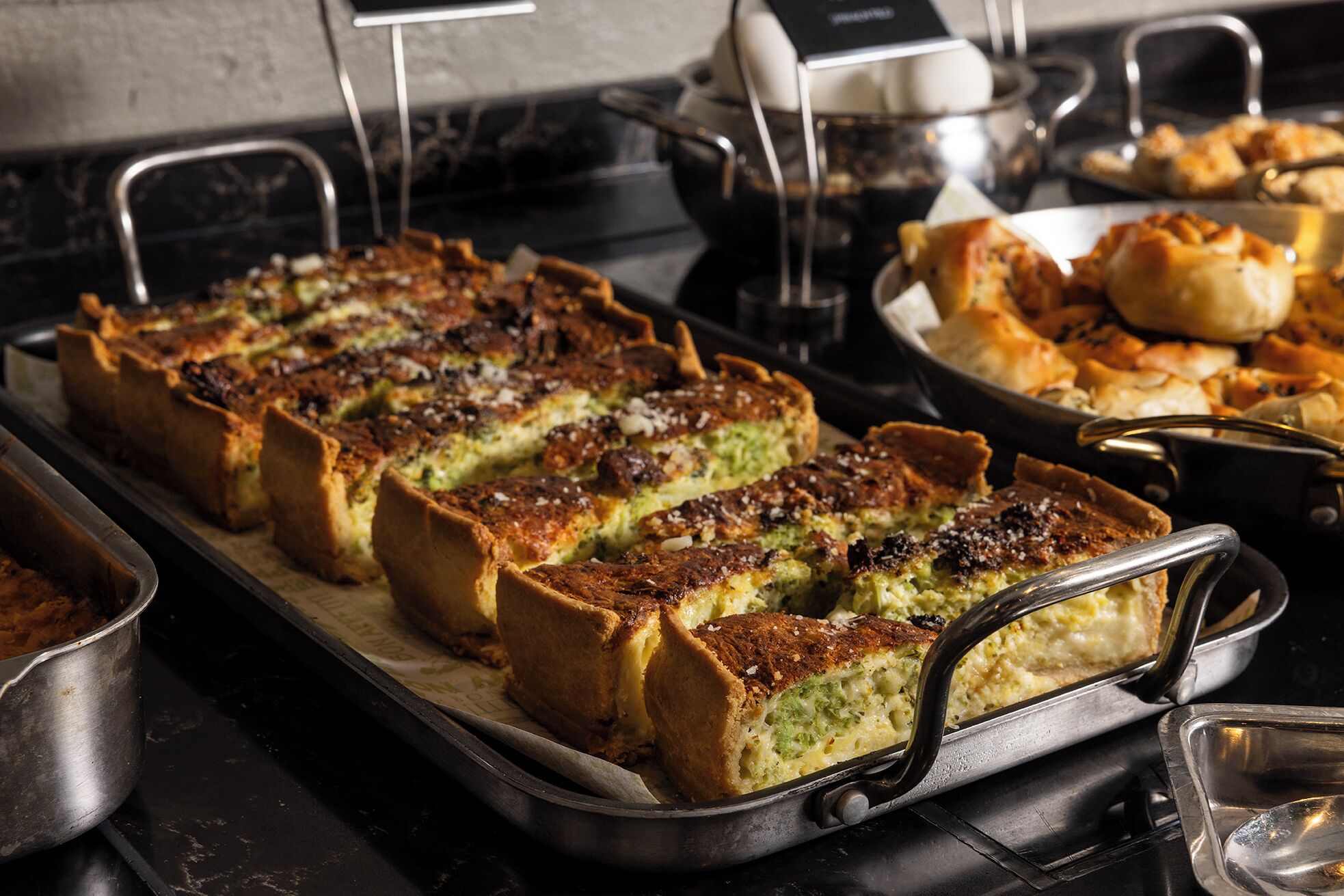Un buffet proposant une variété de plats, notamment un grand plateau de produits de boulangerie et d’autres options alimentaires.