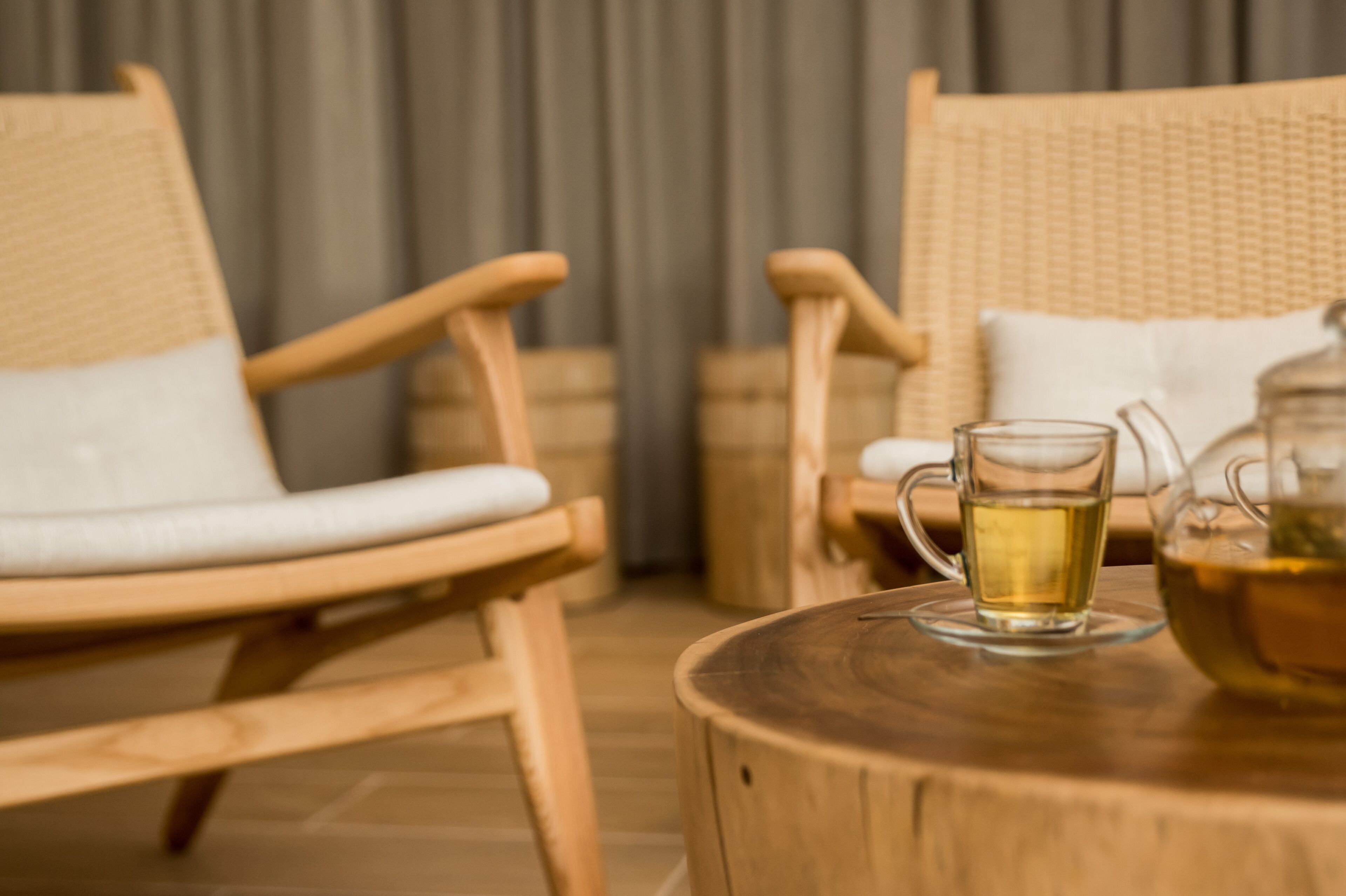Two wicker chairs with white cushions, a round wooden table, and a glass pitcher with a tea cup on it.