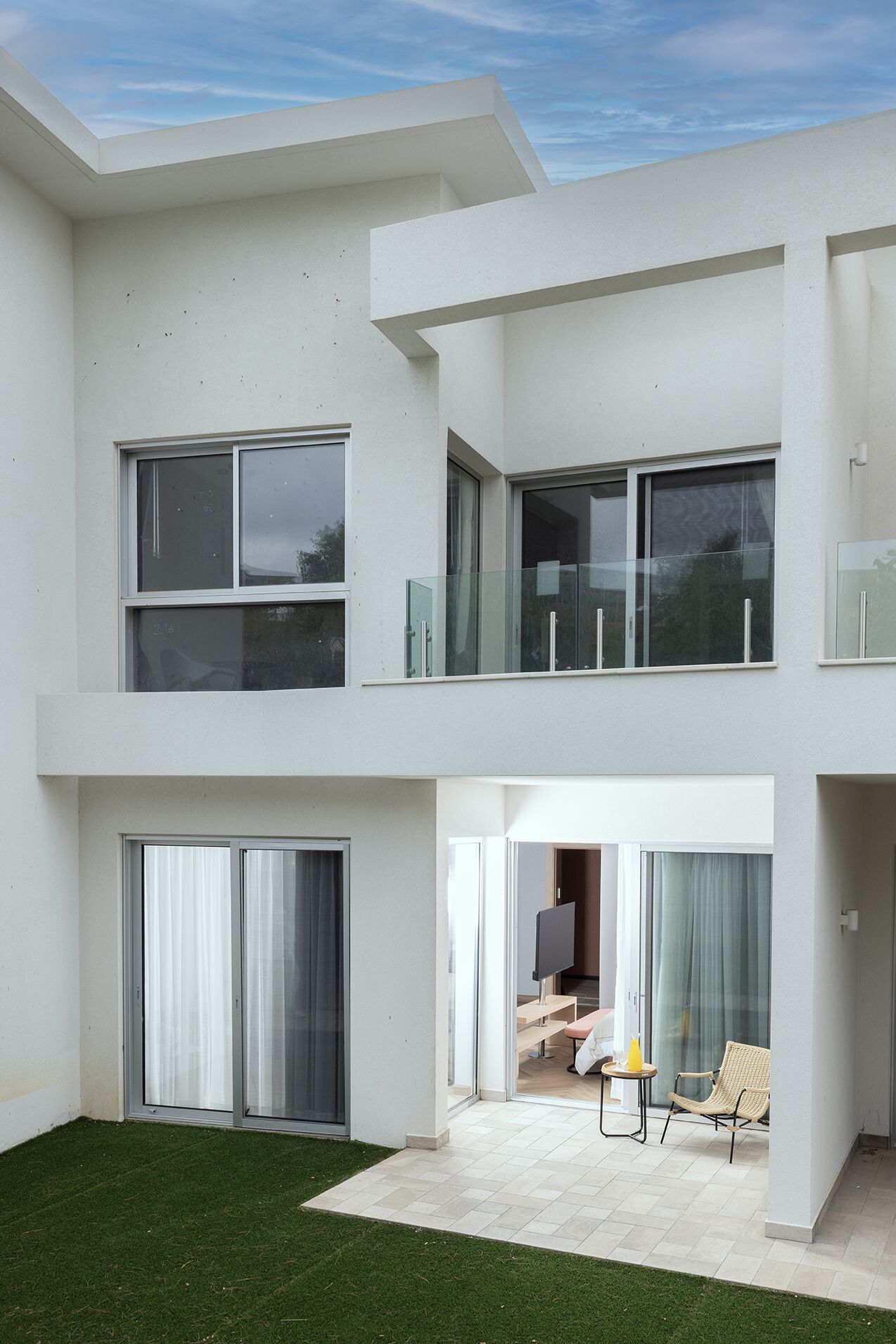 A modern two-story house with large windows, a balcony, and a patio area with outdoor furniture.