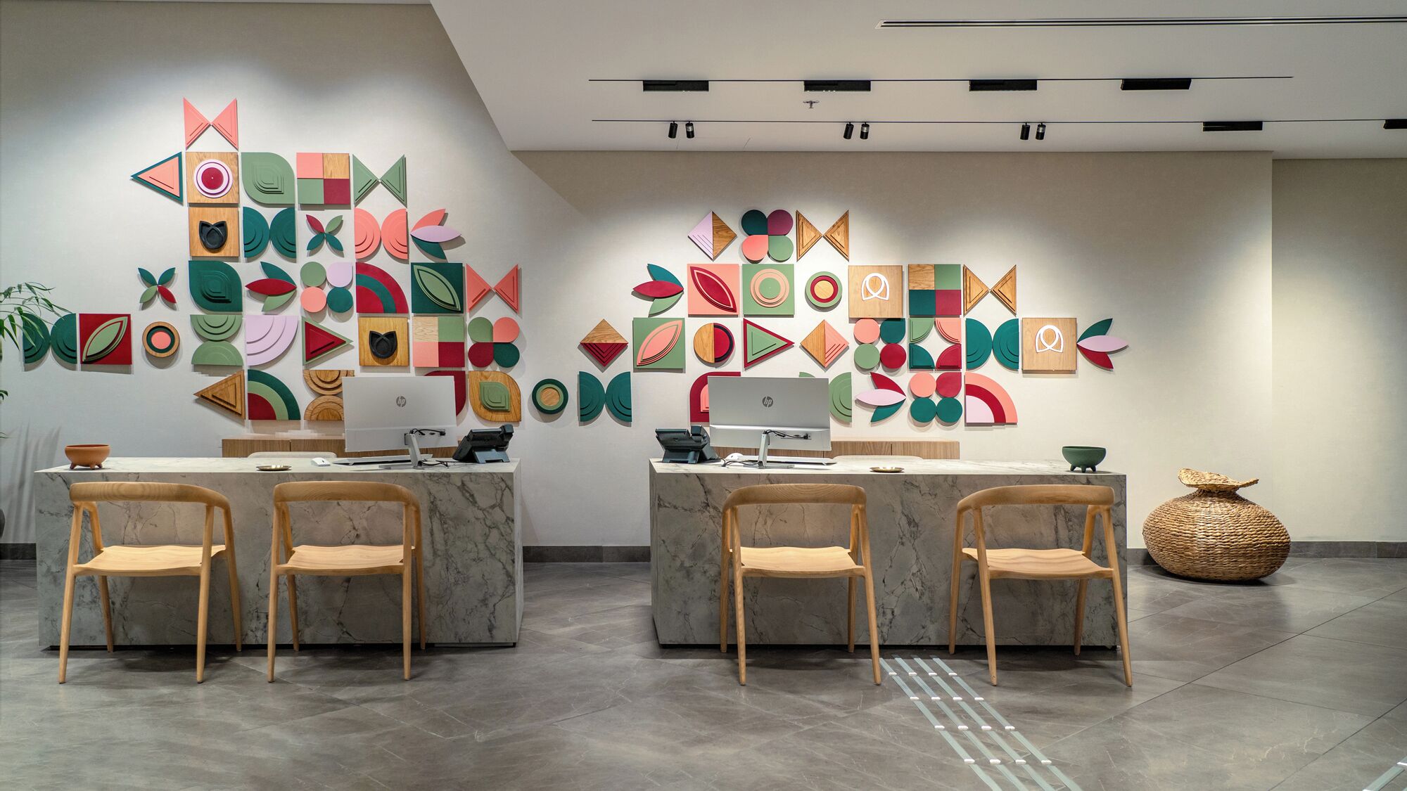 A modern office space with two desks, each with a computer and two chairs. The walls are decorated with colorful geometric wall art.