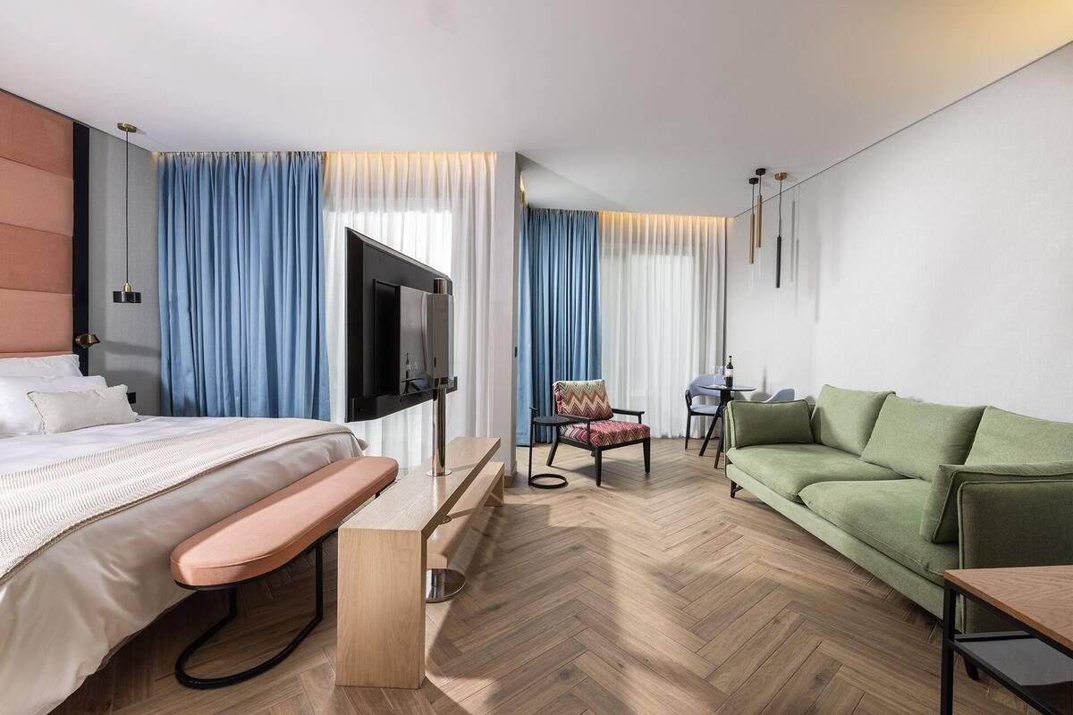 A modern hotel room with a bed, a sofa, a TV, a small table, and a chair.