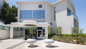 A modern building with a curved entrance, large windows, and a sign reading "ALMOND". - Almond Hotel – Adults Only (Mateh Yehuda)