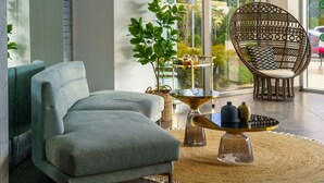 A modern living room with a grey sofa, a wicker chair, and a glass coffee table with decorative items. - Almond Hotel – Adults Only (Mateh Yehuda)