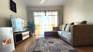 Una sala de estar con sofá, televisión, refrigerador y un ventanal con cortinas.