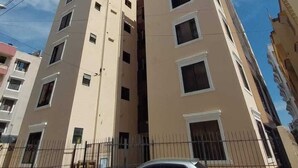Un edificio residencial de varios pisos con fachada color beige, múltiples ventanas y una cerca metálica en primer plano.
