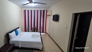 Une chambre à coucher avec un lit, un ventilateur de plafond, une télévision et un rideau à rayures.