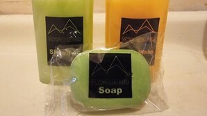 Trois bouteilles de savon, toutes munies d’une étiquette, dont une verte et une orange, sont posées sur une surface.
