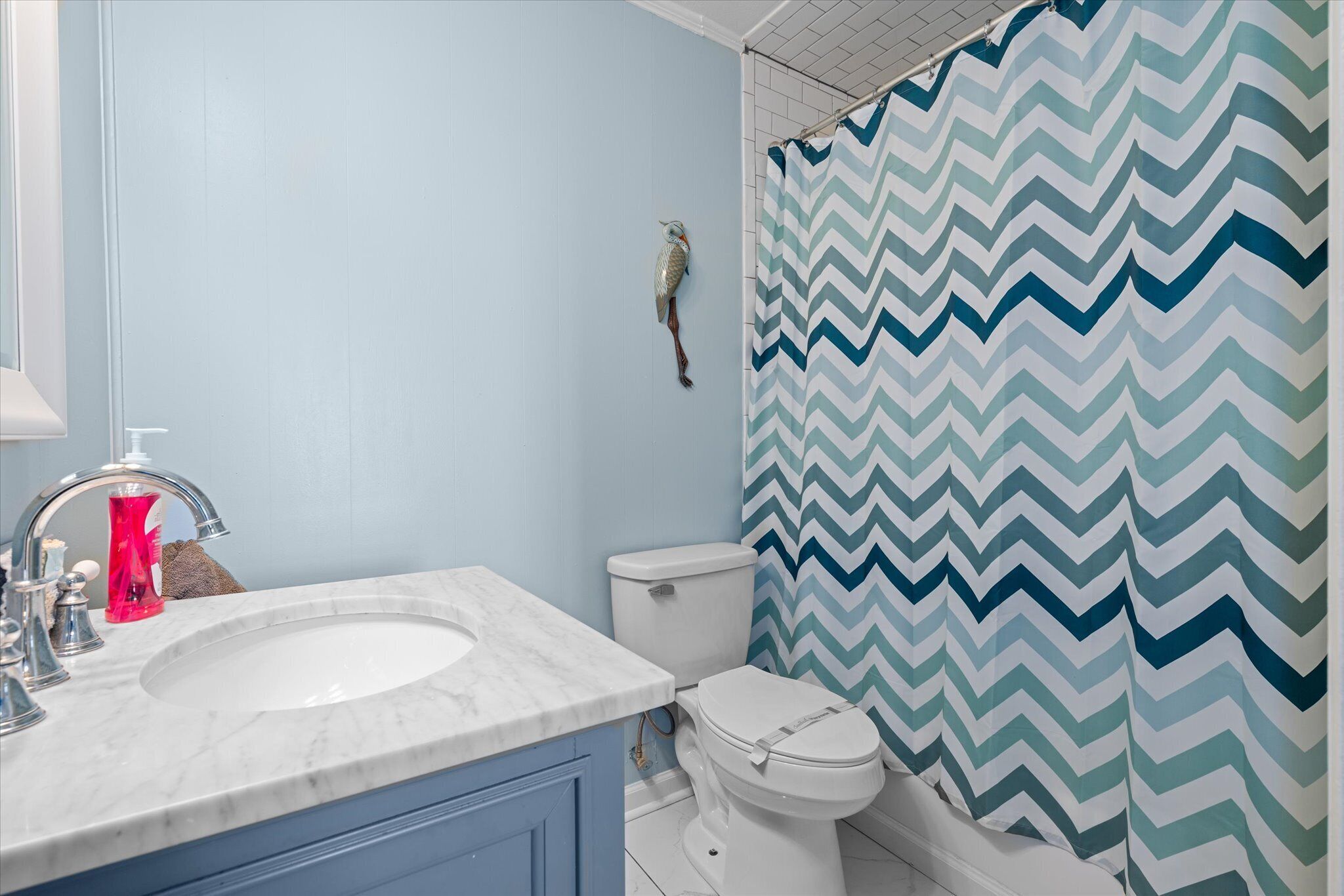 Un baño con un lavamanos blanco, un inodoro y una cortina de ducha con estampado en zigzag.