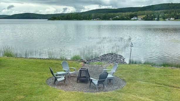 A lakeside seating area with Adirondack chairs and a small table, surrounded by a grassy lawn. - On Long Lake with Direct Access to Trails-L & R Lakeside Rentals  (Sinclair)