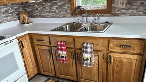 A kitchen with wooden cabinets, a stainless steel sink, and a patterned rug with a bear design. - On Long Lake with Direct Access to Trails-L & R Lakeside Rentals  (Sinclair)