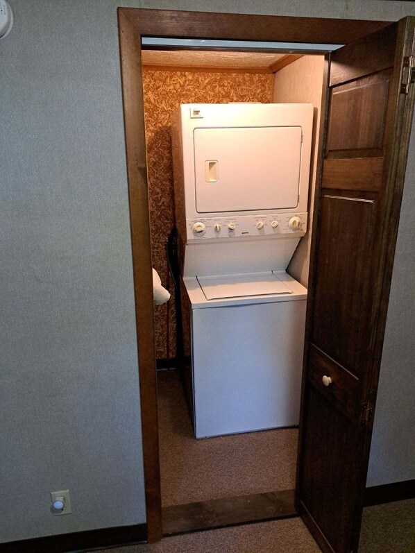 A compact laundry room with a washing machine and dryer, wooden door, and a small towel rack. - On Long Lake with Direct Access to Trails-L & R Lakeside Rentals (Sinclair)