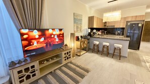 Una cocina moderna con una isla central, taburetes de bar, un refrigerador y un televisor que muestra una escena con velas.