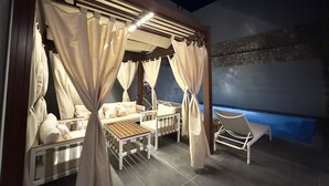 Un espacio de estar al aire libre cubierto, con una mesa y sillas de madera, cojines color beige y un muro de piedra de fondo.