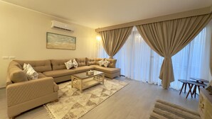 Una sala de estar con un sofá color beige, una mesa de centro de vidrio y una alfombra estampada.