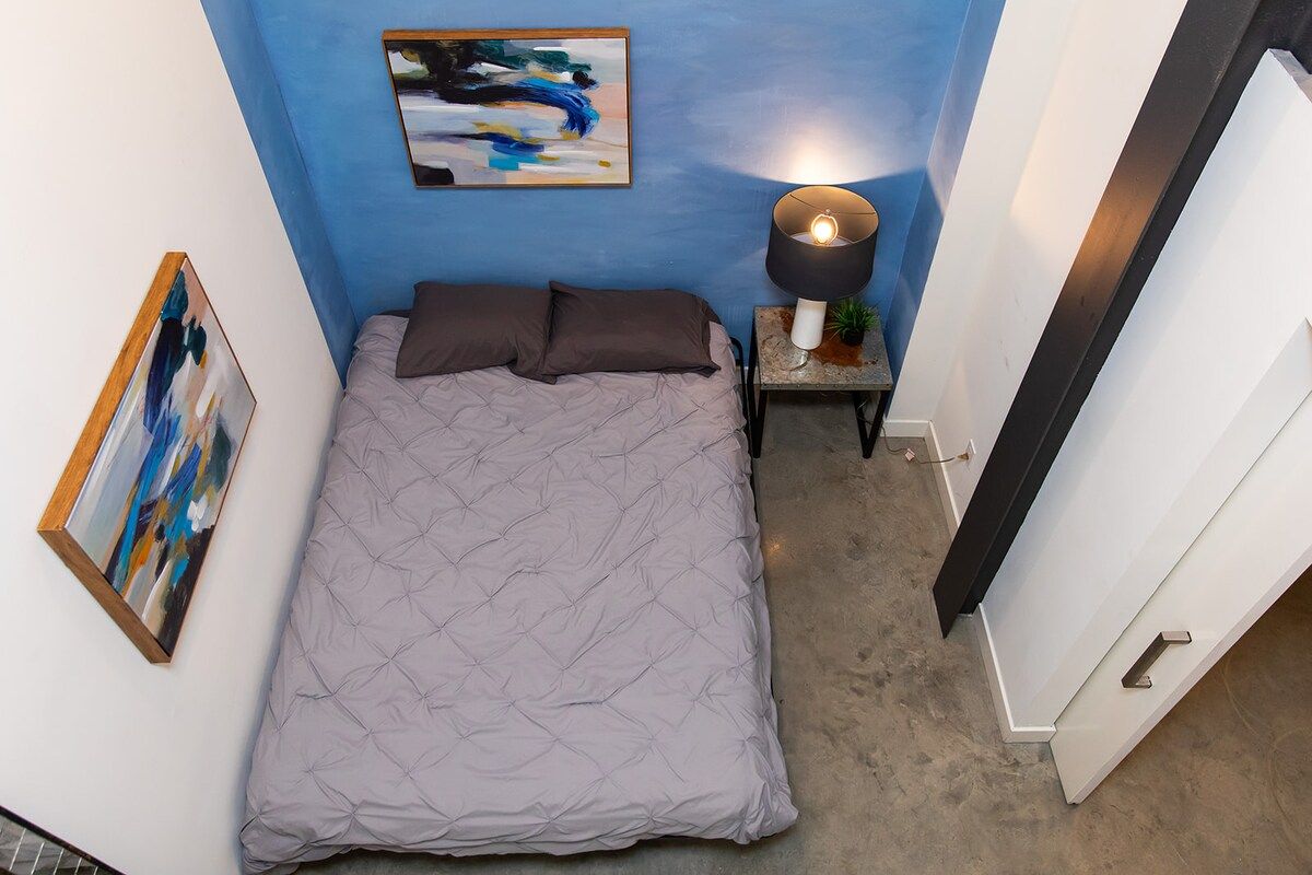 Une chambre à coucher avec un lit, une table de chevet avec une lampe et des œuvres d’art accrochées aux murs.